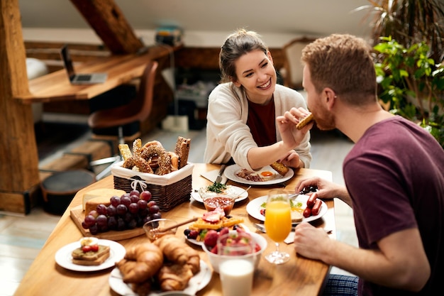 Happy woman feeding her boyfriend during breakfast at dining table