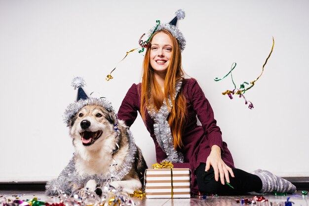 Happy woman in a festive cap sits next to a dog on a gift background