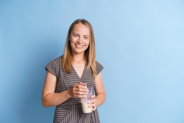 Happy woman in gray dress stands with milkshake in her hands and smiles