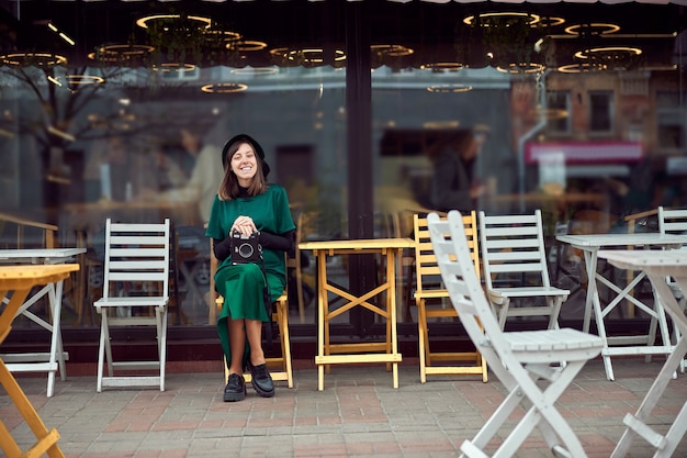 Happy woman in green dress in urban city is sitting near cafe