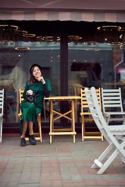 Happy woman in green dress in urban city is sitting near cafe