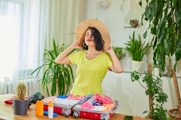 Happy woman in hat dancing packing suitcase getting ready for summer vacation