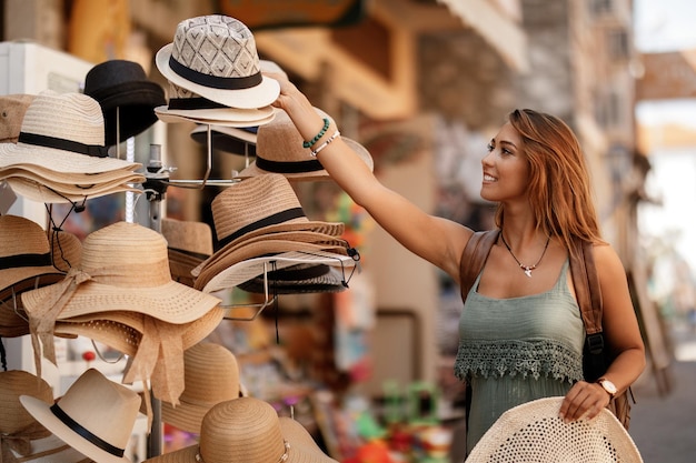 Happy woman having fun on her vacation while buying sun hat on street market