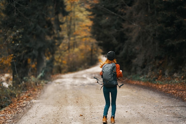 Happy woman hiker with backpack walks on the road in autumn forest