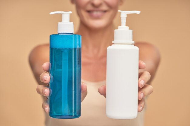 Happy woman holding bottles with natural skincare product in studio