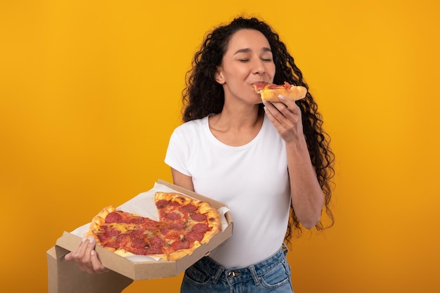 Happy woman holding box eating pizza at studio