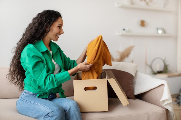 Happy woman holding clothes unpacking cardboard box at home