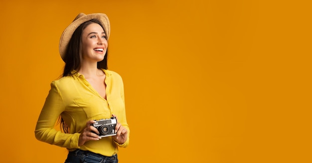 Happy Woman Holding Retro Camera Standing Over Yellow Studio Background