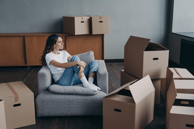 Happy woman is an apartment buyer Mover is dreaming among boxes in living room of new home