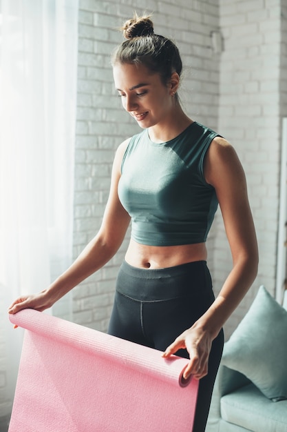 Happy woman is finishing her fitness training session gathering her mat from the floor