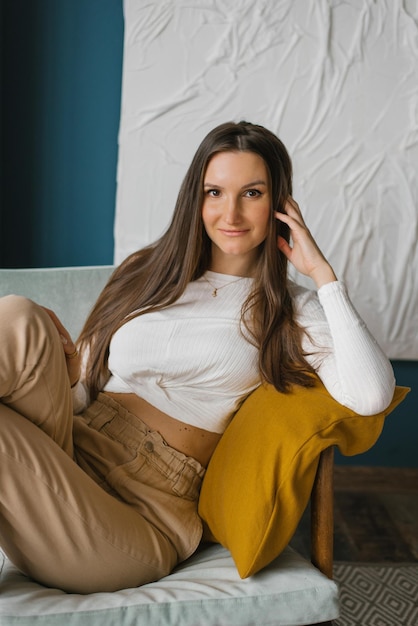 Happy woman is sitting on a chair at home leaning on her arm