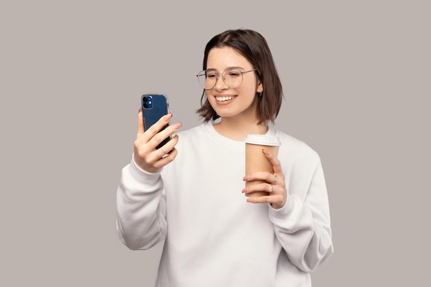 Happy woman is texting on the phone while holding a take away coffee cup