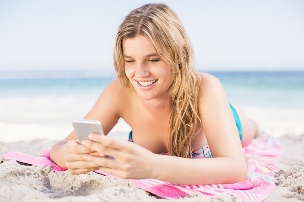 Happy woman lying on the beach and using mobile phone