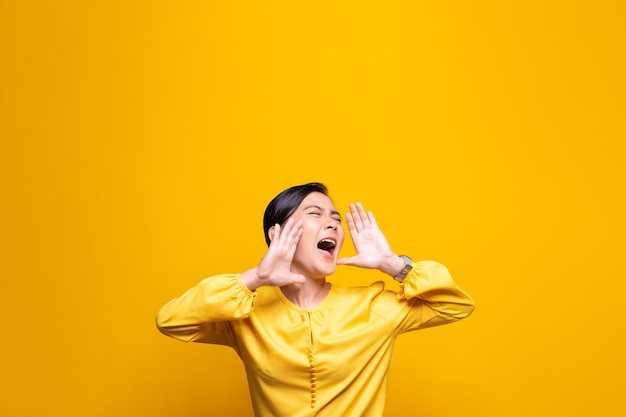 Happy woman making shout gesture isolated over yellow wall