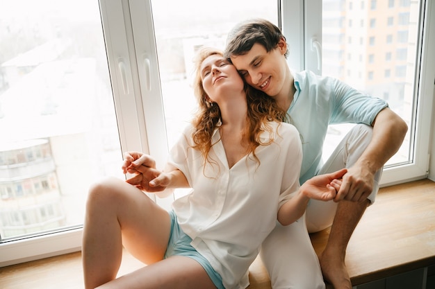 Happy woman and man hugging near window in home on Valentine Day