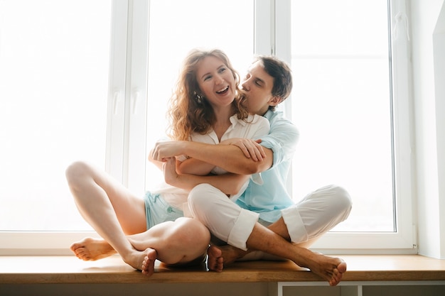 Happy woman and man hugging near window in home on Valentine Day