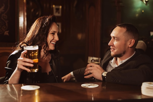 Happy woman and a man with glasses of draft beer chat and smile behind the bar counter