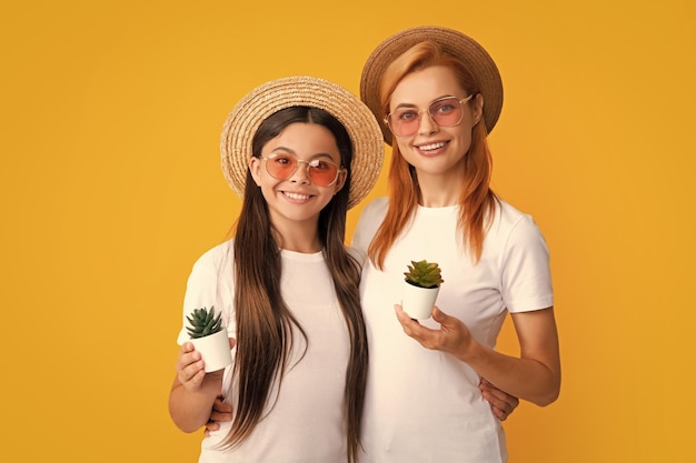 Happy woman mother and daughter child holding pot plant on yellow isoalted background