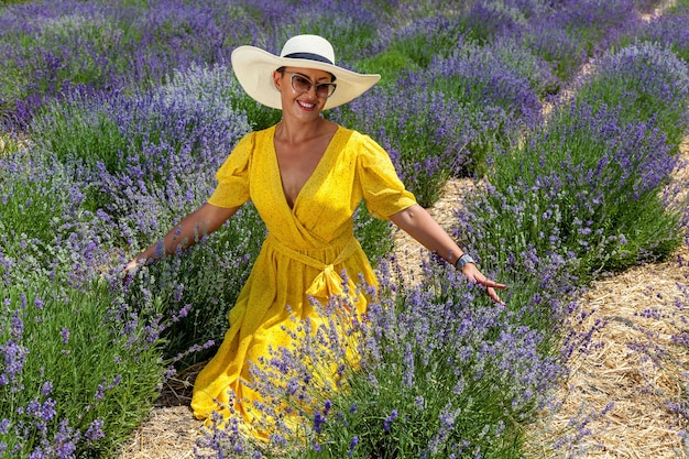 Happy woman near flowering bush lavender. Portrait of young smiling beautiful woman in yellow dress,