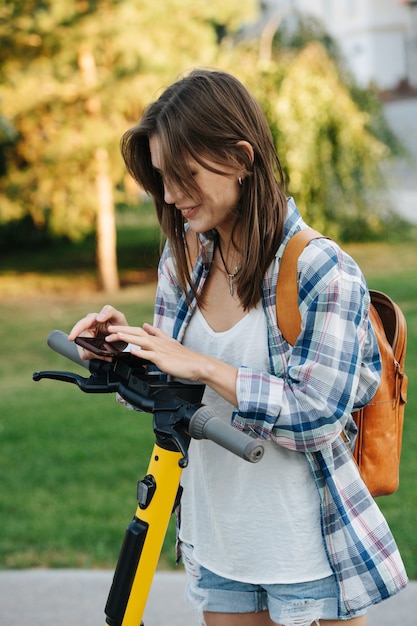 Happy woman in the park paying for her electric scooter with a phone app