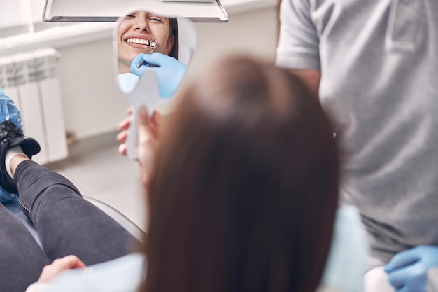 Photo happy woman patient is looking in mirror on her teeth and smiling