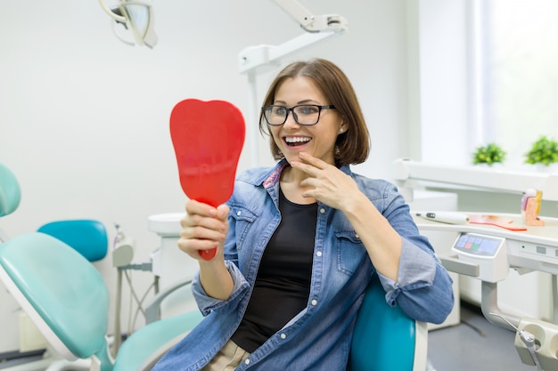 Happy woman patient looking in the mirror at the teeth