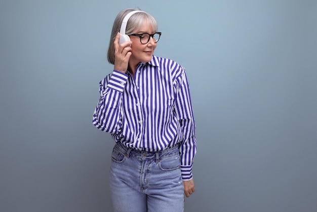 Happy woman pensioner with gray hair with headphones on a bright studio background