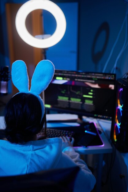 Happy woman putting on headphones and playing computer game Female gamer in glasses sitting and looking at computer monitor