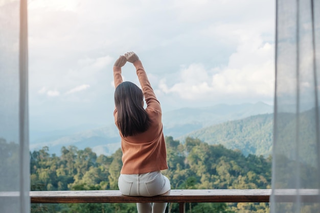 Happy woman relaxing and looking mountain view at countryside home or homestay in the morning Vacation blogger SoloTravel journey trip and relaxing concept