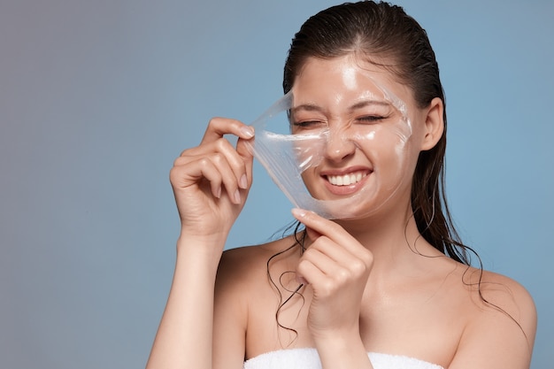 Happy woman removing with hardness her facial mask and smiling