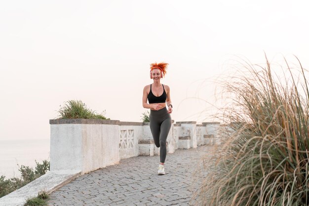 Happy woman runner jogging on footpath under clear sky