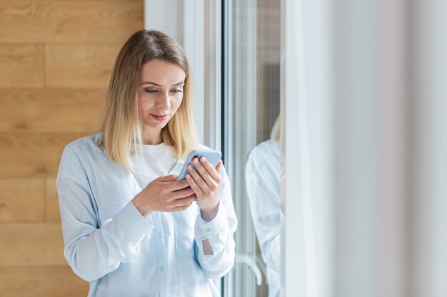 happy woman saw the good news on smartphone standing by the window in office or at home indoors