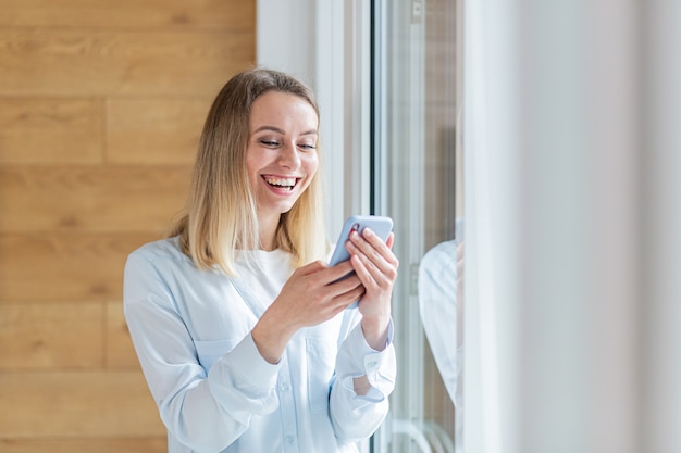 happy woman saw the good news on smartphone standing by the window in office or at home indoors