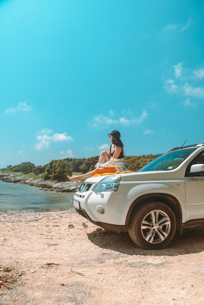 Happy woman at sea summer beach sitting at car hood