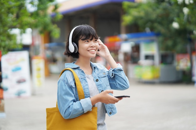 Happy woman shopping with listening to music on smartphone and holding tote bag