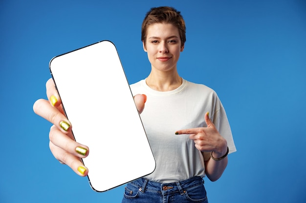 Happy woman shows blank smartphone screen against blue background