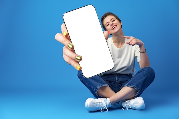 Happy woman shows blank smartphone screen against blue background