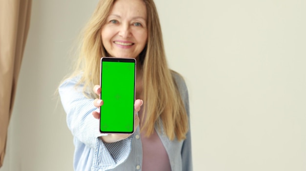 A happy woman shows a phone with a green screen Template