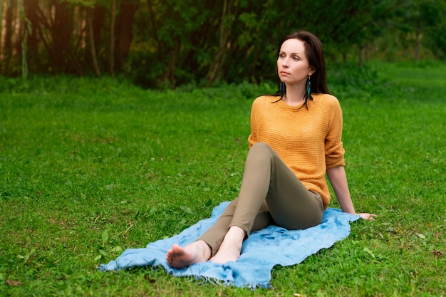 Happy woman sitting on the grass in the Park resting