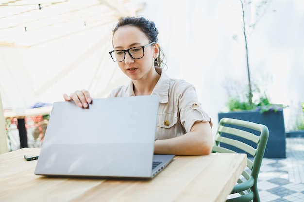 Happy woman sitting at outdoor cafe table and talking on phone with cup of coffee smiling woman enjoying telecommuting in cafe or studying online