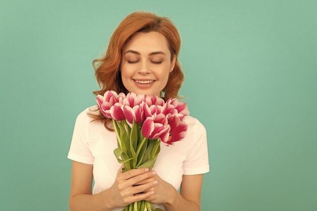 Happy woman smelling tulip flower bouquet on blue background