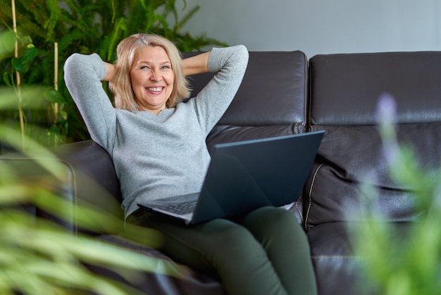 Happy woman on a sofa at home concentrating as she works on a laptop.