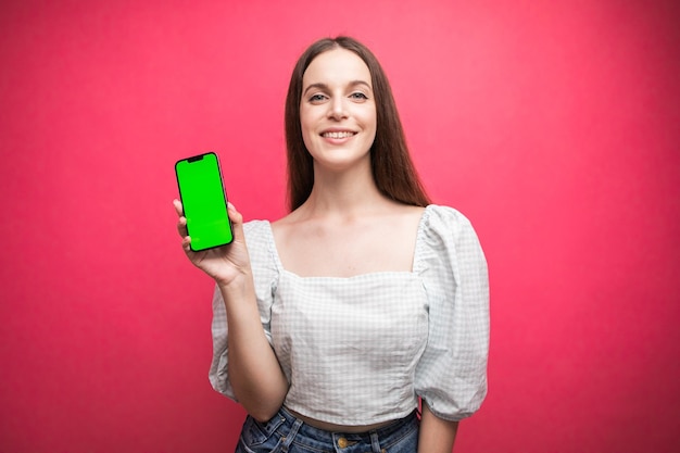 Happy woman standing and hold smartphone on pink background. Green screen phone screen