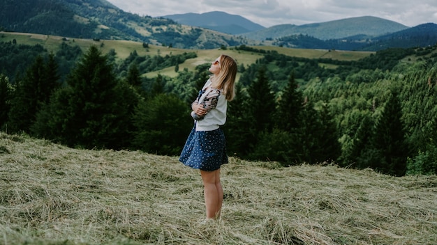 Photo happy woman standing on the mountain top looking at panoramic view of mountain range under blue sky