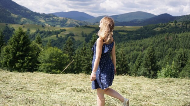 Photo happy woman standing on the mountain top looking at panoramic view of mountain range under blue sky