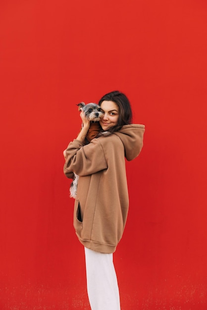 Happy woman stands on a background of a red wall with a funny cute dog looks at the camera