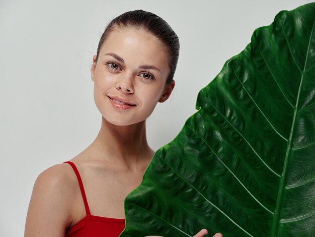 Happy woman stands behind palm leaf on light background red swimsuit clean skin isolated