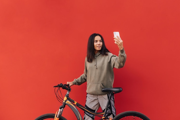 Happy woman in stylish dressed clothes stands with a bicycle on a background of red wall