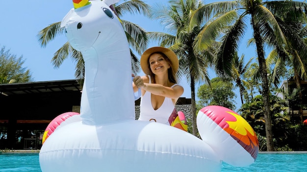 Happy woman in swimwear fun and dancing on floaties inflatable unicorn mattress