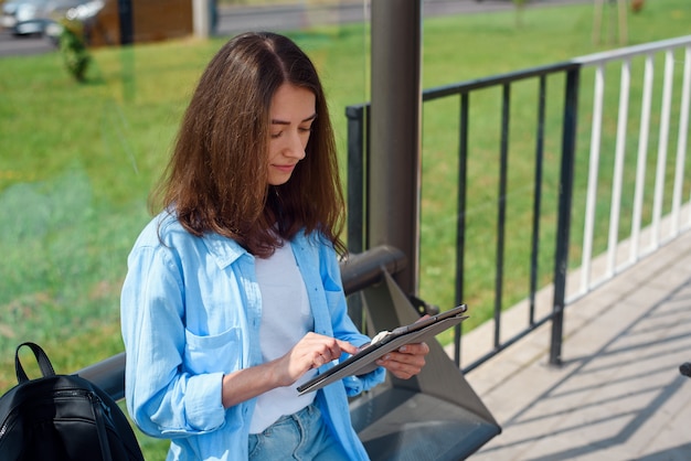 Happy woman uses a tablet or ebook on a tram station while waiting for public transport.